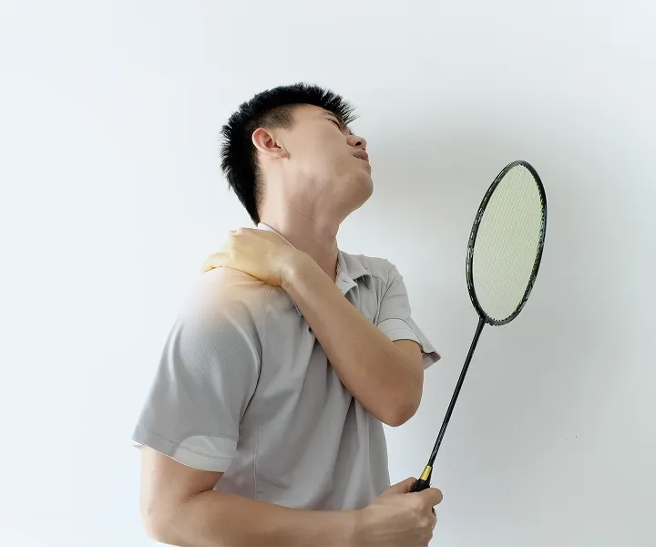 Badminton player holding a painful shoulder after play, illustrating a sports-related shoulder injury.