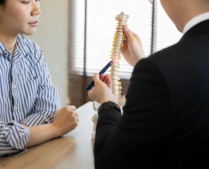Dr Seng Chusheng pointing with a pen to a model of the human spine while consulting a female patient.