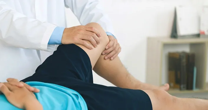 Orthopaedic specialist performing a physical examination of a patient's knee during a consultation in Singapore.
