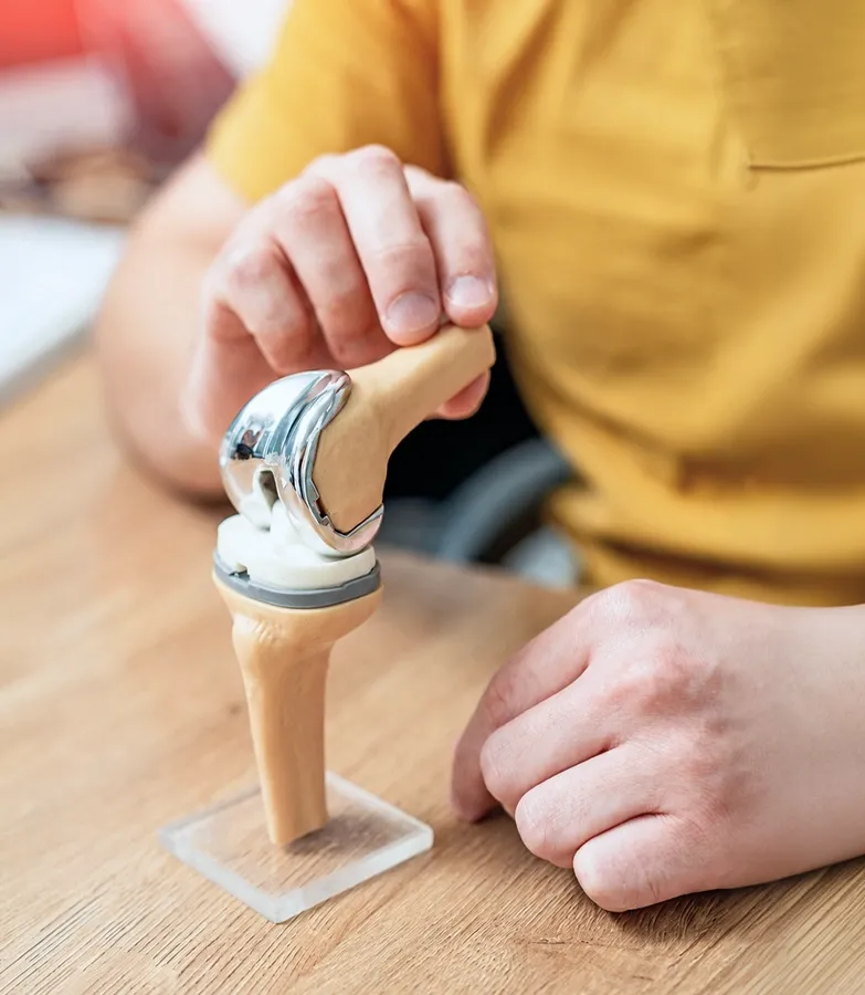 Patient holding a knee replacement implant model during an orthopaedic consultation in Singapore.