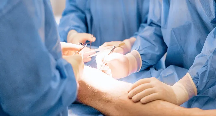 Orthopaedic surgeon performing a knee surgery procedure in an operating theatre.
