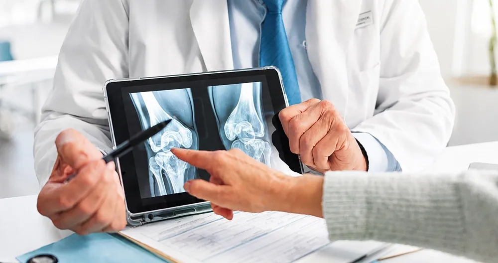 Orthopaedic doctor explaining knee X-ray results to a patient during a consultation.