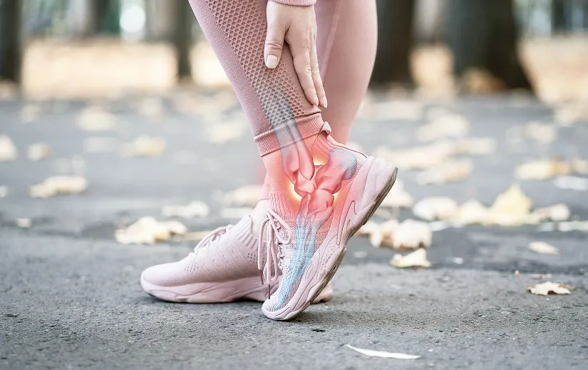 An athlete wearing pink running shoes clutching their ankle, featuring an overlay graphic showing inflamed leg and foot bones.