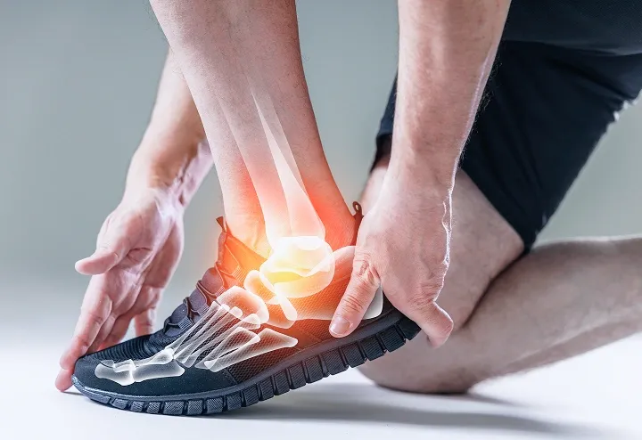An athlete in running shoes holding a painful ankle, with a digital skeleton overlay and a red glow indicating an ankle sprain.