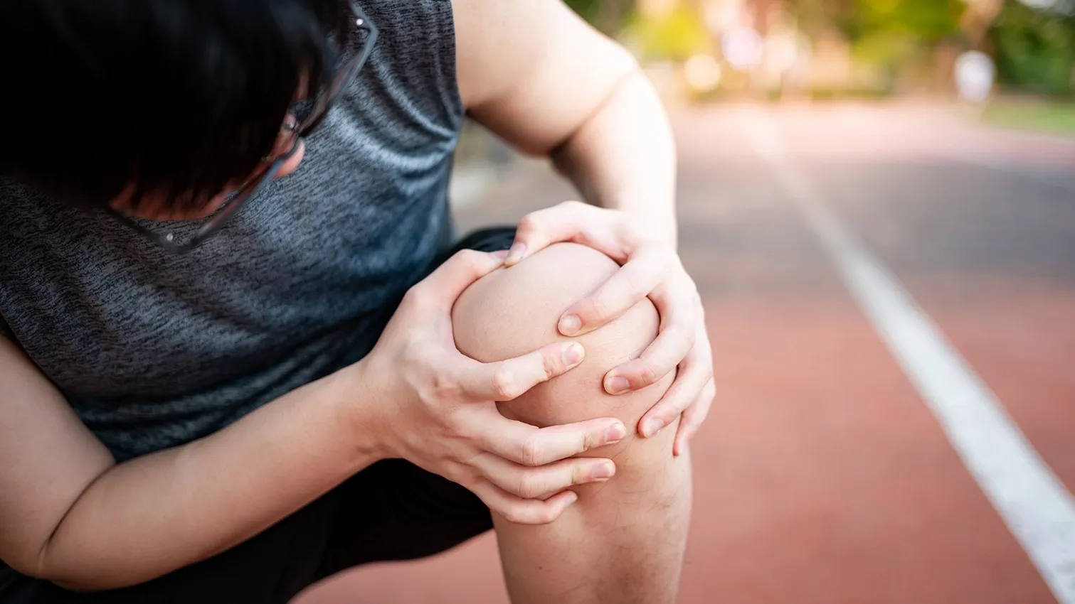 Person holding a painful knee after a running-related sports injury on an outdoor track.
