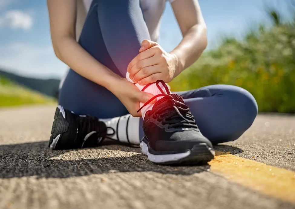 An athlete sitting on an asphalt path holding a painful ankle injury, with a subtle red glow highlighting the sprain.