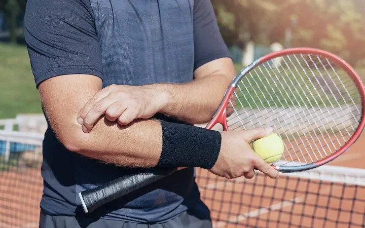 Tennis player holding a tennis racket and ball while pressing a painful elbow.