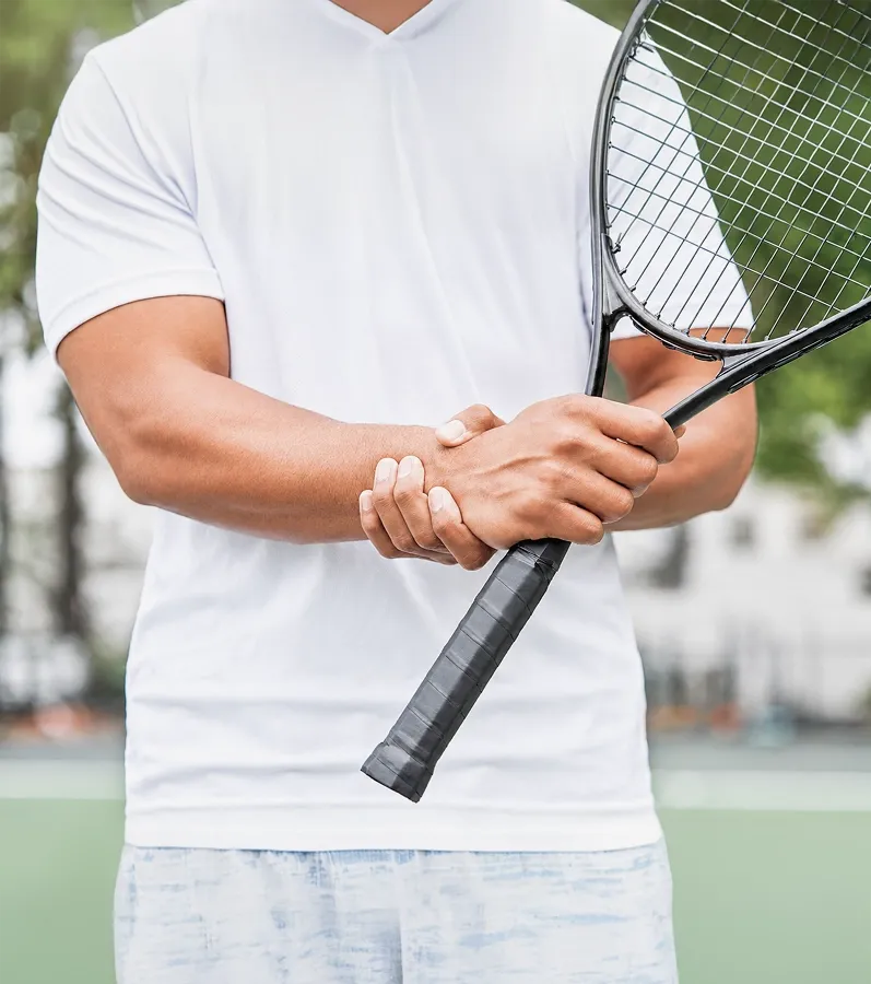 A tennis player in a white shirt holding his painful wrist while gripping a tennis racket on a court.